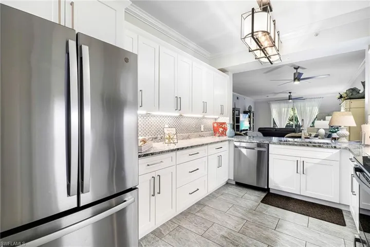 Kitchen with decorative backsplash, white cabinets, light stone countertops, and appliances with stainless steel finishes