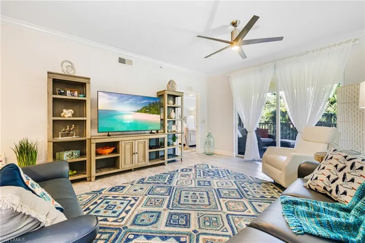 Living room with ceiling fan, tile patterned flooring, and ornamental molding