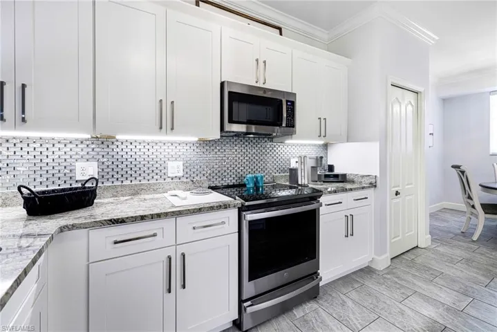 Kitchen with white cabinets, backsplash, stainless steel appliances, and light stone countertops