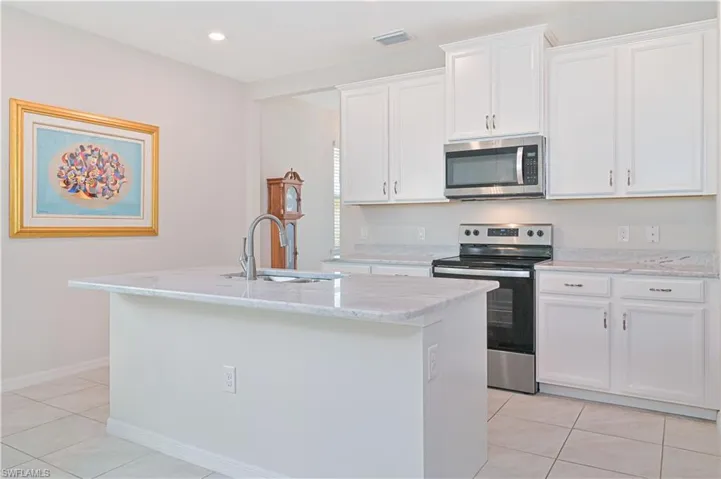 Kitchen with appliances with stainless steel finishes, light tile patterned floors, an island with sink, white cabinets, and light stone counters