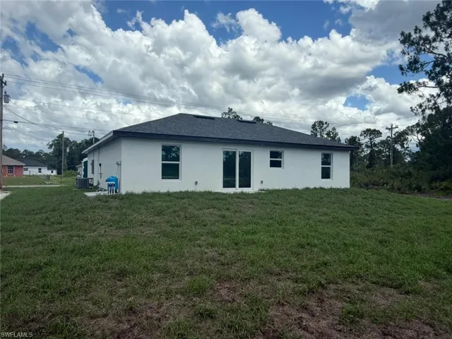 Back of property featuring stucco siding, a lawn, and a shingled roof