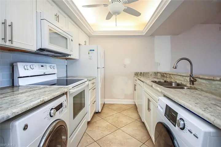 Kitchen featuring white appliances, washer / dryer, a sink, and a tray ceiling