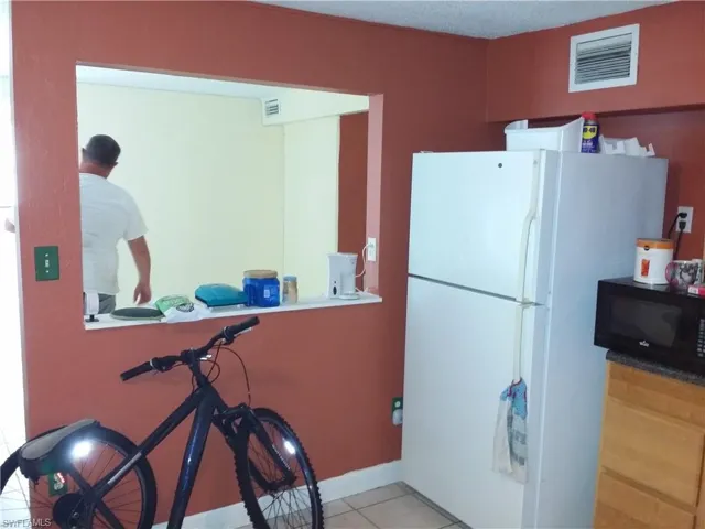 Kitchen featuring freestanding refrigerator, black microwave, a textured ceiling, and dark countertops