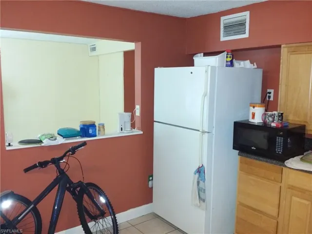 Kitchen with freestanding refrigerator, black microwave, light tile patterned floors, and a textured ceiling