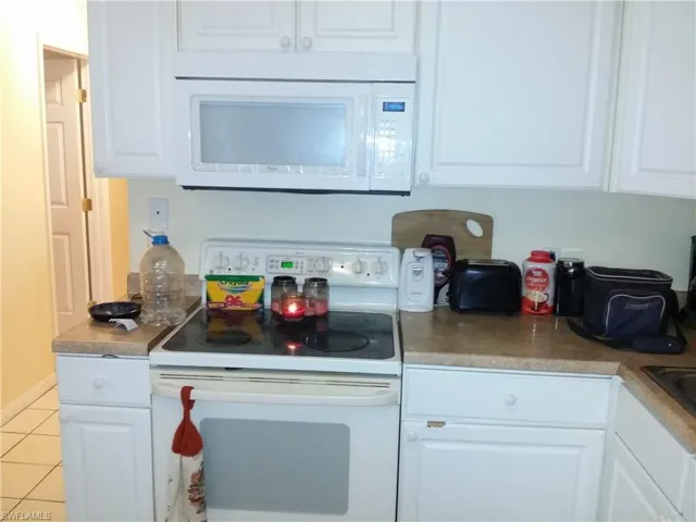 Kitchen with white appliances, white cabinetry, light tile patterned floors, and light countertops