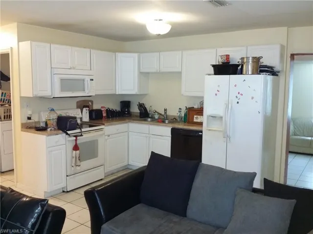 Kitchen featuring light tile patterned floors, white appliances, white cabinetry, washer / clothes dryer, and open floor plan