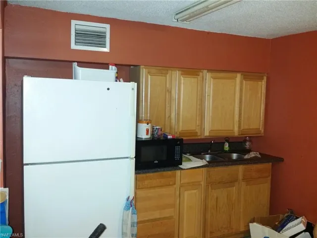 Kitchen with freestanding refrigerator, black microwave, a textured ceiling, and dark stone countertops