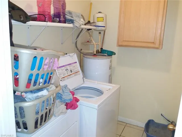 Laundry area with light tile patterned flooring, water heater, cabinet space, and separate washer and dryer