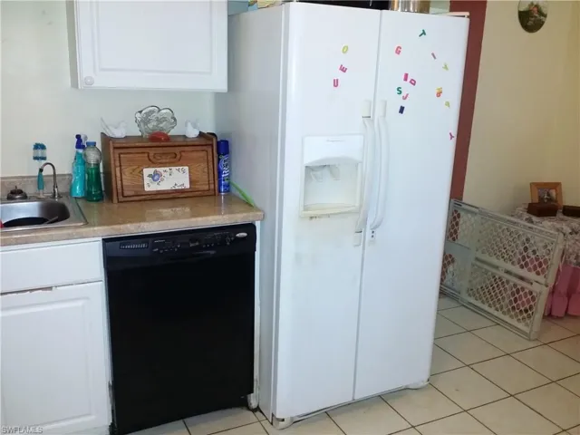 Kitchen featuring white cabinets, white refrigerator with ice dispenser, light countertops, black dishwasher, and light tile patterned floors