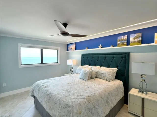 Master bedroom featuring a tufted upholstered headboard in deep teal, tile flooring throughout, and a ceiling fan with integrated lighting