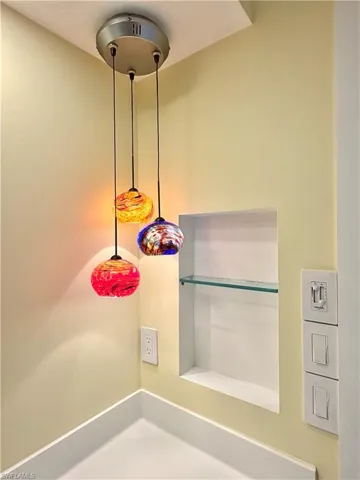 Custom lighting fixture with three colorful glass pendant lights, built-in wall niche with a glass shelf, and a white countertop surface