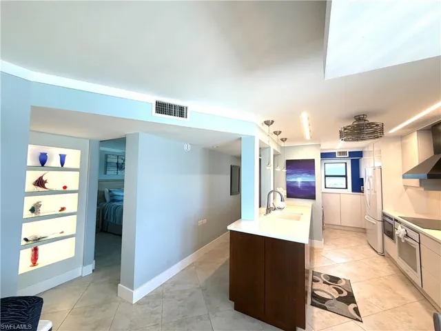 Contemporary kitchen featuring a large waterfall-edge island with wood-finish cabinetry, stainless steel appliances, quartz countertops, and tile flooring
