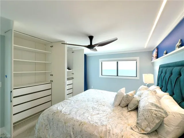 Built-in white cabinetry with drawers and shelving, ceiling fan, window with exterior exposure, recessed ceiling lighting, and a tufted upholstered headboard