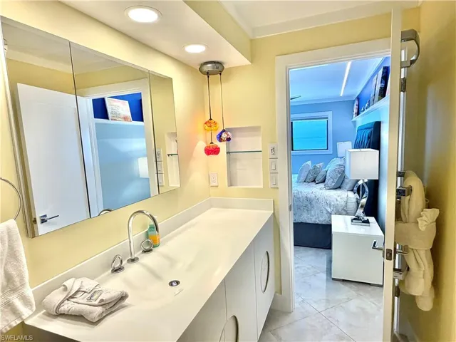 Spa-inspired ensuite bathroom featuring a large framed mirror, white vanity with integrated sink, polished chrome faucet, glass art pendant lighting, tile flooring, and direct access to the primary bedroom suite