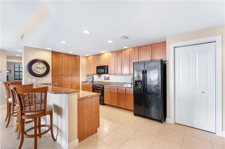 Kitchen featuring brown cabinetry, a kitchen bar, black appliances, and light stone countertops