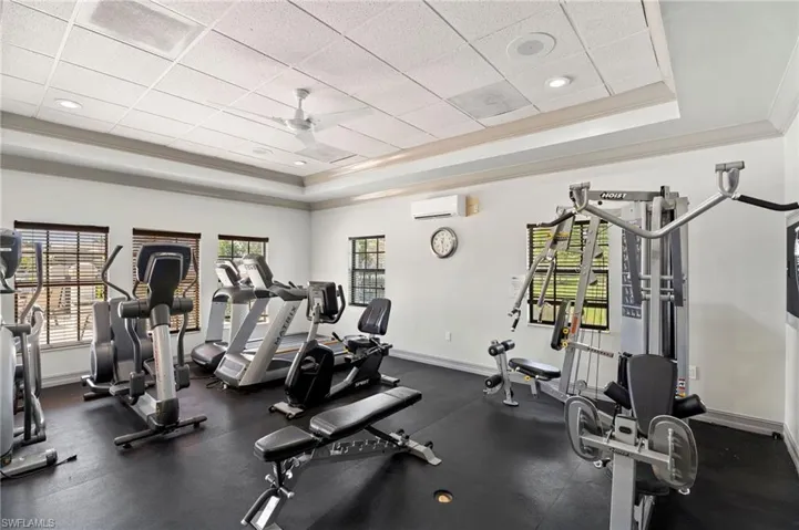 Gym with a wall unit AC, baseboards, a tray ceiling, and a drop ceiling