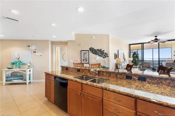 Kitchen with a sink, stone counters, open floor plan, and dishwasher