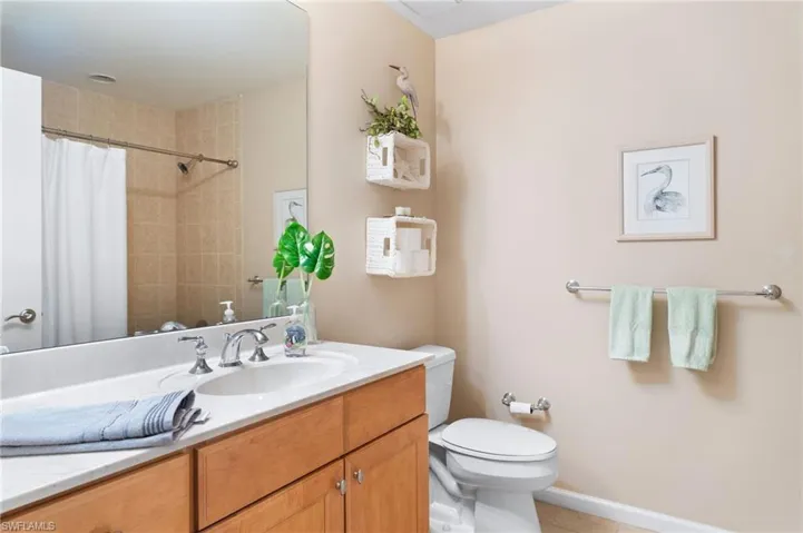 Full bath featuring curtained shower, toilet, vanity, baseboards, and tile patterned floors
