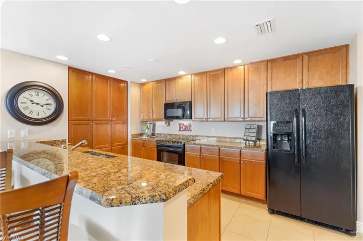 Kitchen with a peninsula, a sink, visible vents, black appliances, and brown cabinetry