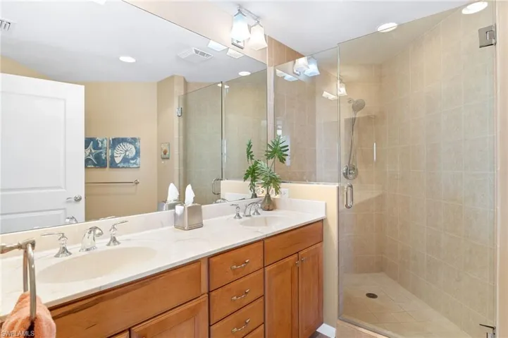 Full bath with visible vents, a sink, a shower stall, and double vanity