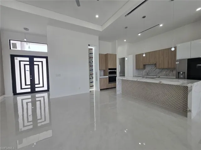 Kitchen featuring modern cabinets, light stone counters, pendant lighting, wood finish cabinets, and a high ceiling