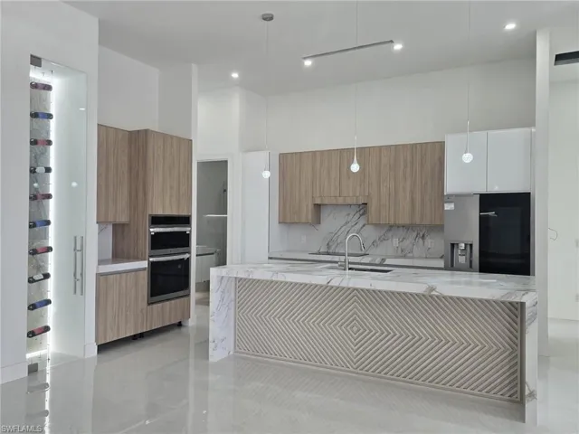 Kitchen featuring light stone counters, modern cabinets, pendant lighting, stainless steel appliances, and an island with sink