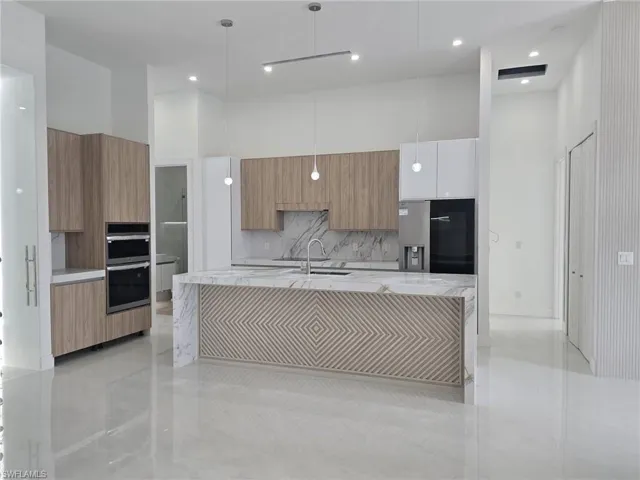 Kitchen featuring light stone countertops, modern cabinets, a center island with sink, decorative light fixtures, and a high ceiling