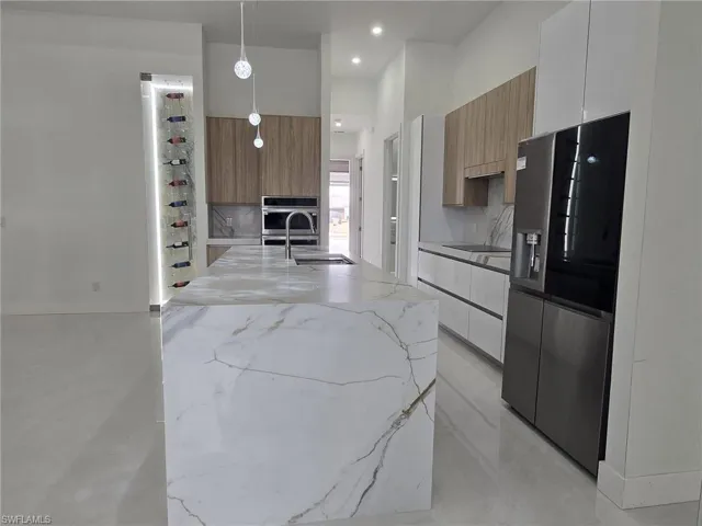 Kitchen featuring light stone counters, modern cabinets, hanging light fixtures, stainless steel appliances, and a high ceiling