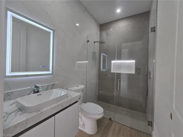 Bathroom with vanity, a marble finish shower, recessed lighting, stone wall, and tile walls