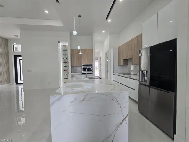 Kitchen featuring stainless steel appliances, modern cabinets, light stone countertops, and decorative light fixtures