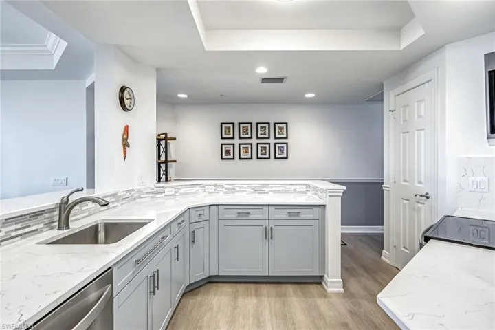 Kitchen featuring a raised ceiling, gray cabinets, light stone countertops, light wood-type flooring, and recessed lighting