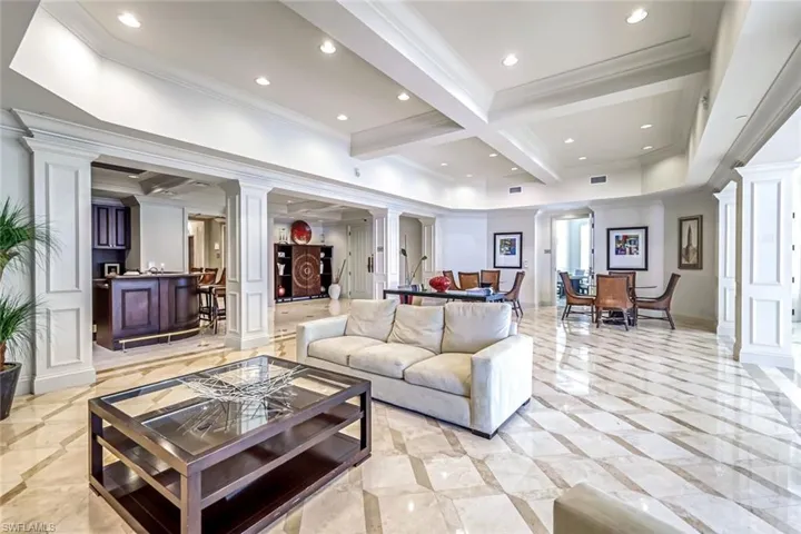Living room featuring ornate columns, beam ceiling, coffered ceiling, inlaid floor details, and ornamental molding