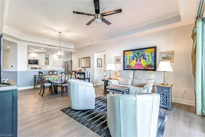 Living area with a raised ceiling, ornamental molding, light wood-style flooring, and ceiling fan