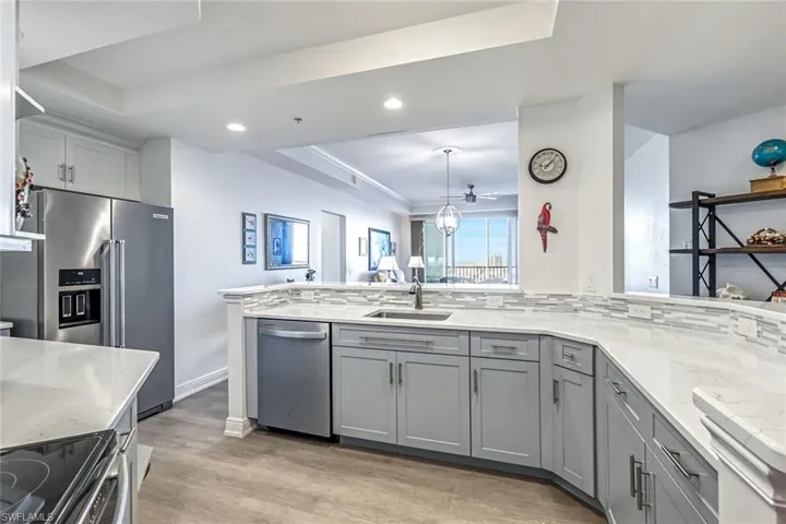 Kitchen featuring a tray ceiling, gray cabinets, a peninsula, appliances with stainless steel finishes, and light stone counters