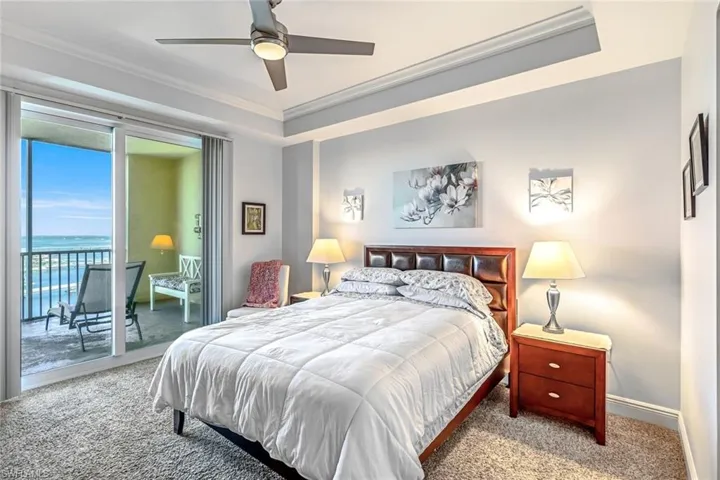 Carpeted bedroom featuring access to outside, a ceiling fan, crown molding, and a tray ceiling