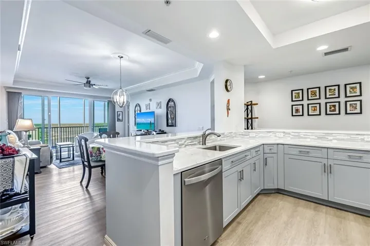 Kitchen with dishwasher, light wood finished floors, a tray ceiling, gray cabinetry, and light stone counters