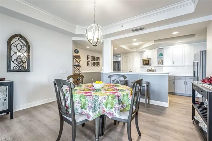 Dining room with a tray ceiling, light wood-type flooring, ornamental molding, and recessed lighting