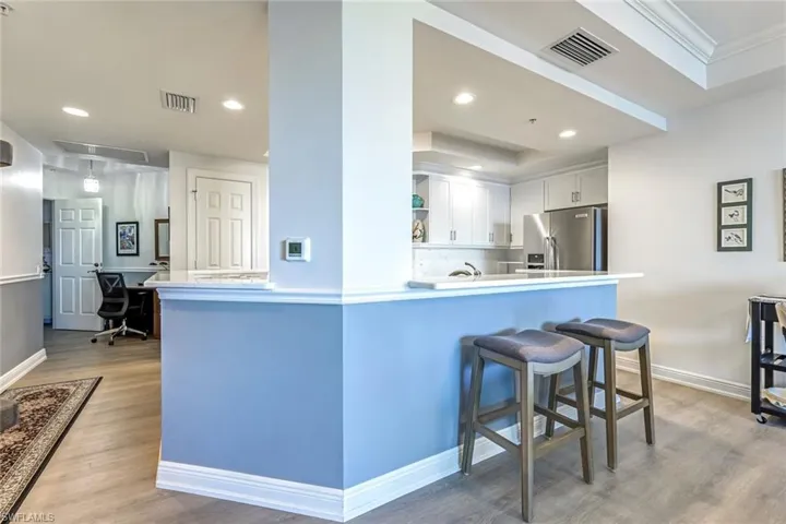 Kitchen with a desk, light wood-style floors, stainless steel fridge with ice dispenser, open shelves, and a kitchen breakfast bar