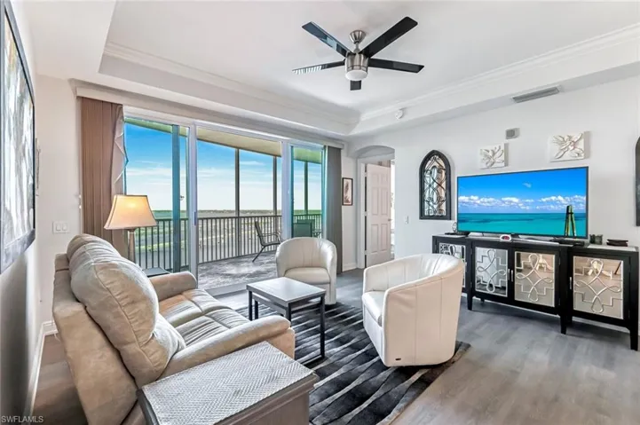 Living area with a raised ceiling, wood finished floors, crown molding, arched walkways, and a ceiling fan