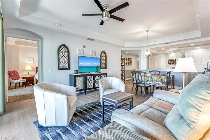 Living area featuring a tray ceiling, ornamental molding, wood finished floors, arched walkways, and ceiling fan