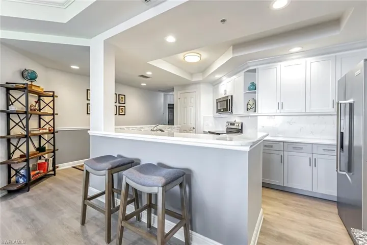 Kitchen with open shelves, a tray ceiling, tasteful backsplash, a breakfast bar area, and light wood finished floors