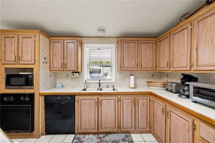 Kitchen featuring sink, light tile patterned flooring, black appliances, and a textured ceiling