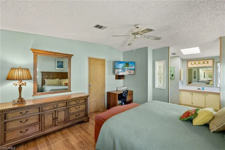 Bedroom featuring ensuite bathroom, a skylight, ceiling fan, a textured ceiling, and light hardwood / wood-style floors