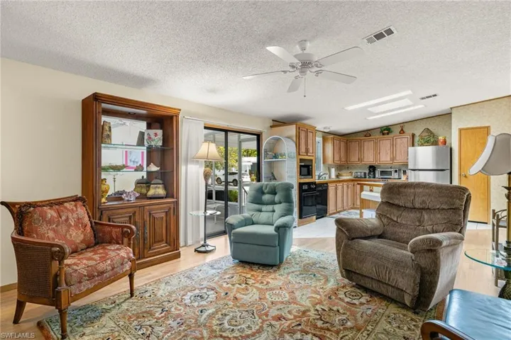 Living room with a textured ceiling, light wood-type flooring, vaulted ceiling, and ceiling fan