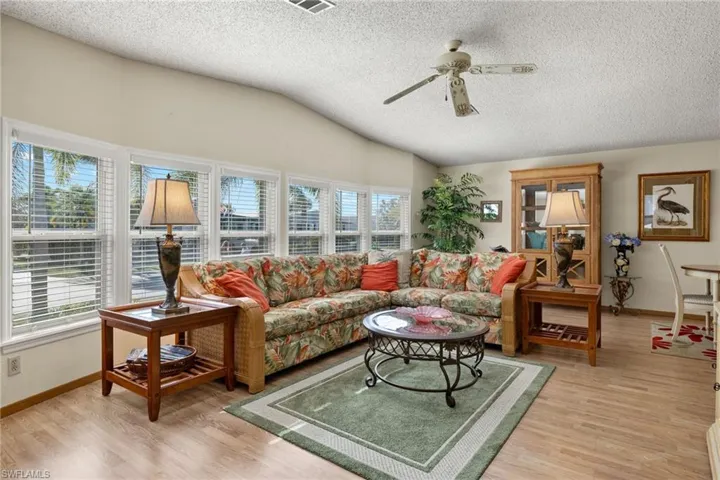 Living room featuring a textured ceiling, ceiling fan, vaulted ceiling, and light wood-type flooring