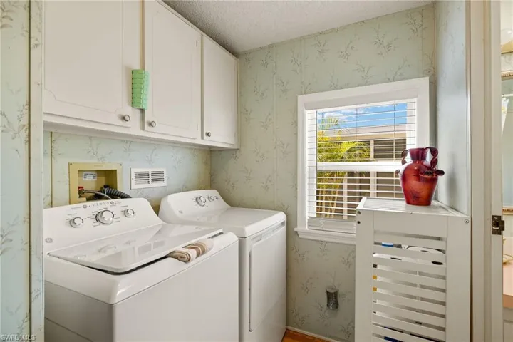 Laundry room featuring washing machine and clothes dryer, cabinets, and a textured ceiling