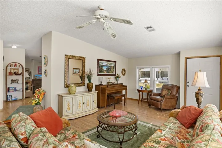 Living room featuring a textured ceiling, light hardwood / wood-style floors, vaulted ceiling, and ceiling fan