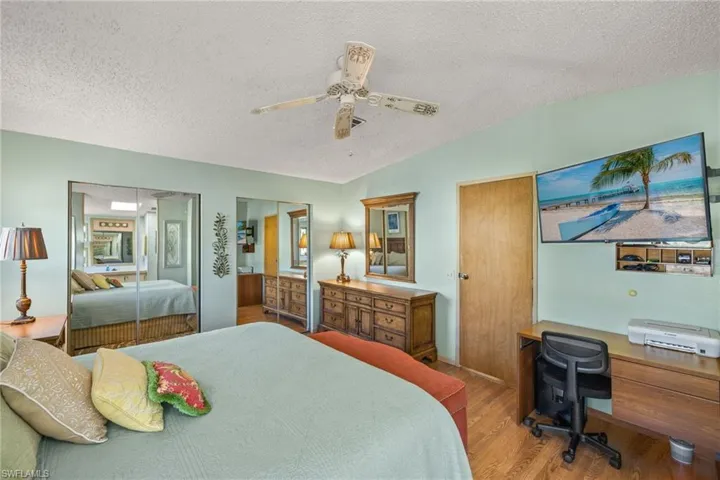 Bedroom with hardwood / wood-style floors, lofted ceiling, ceiling fan, a textured ceiling, and multiple closets