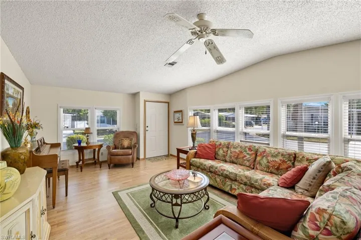 Living room featuring a textured ceiling, light hardwood / wood-style flooring, ceiling fan, and lofted ceiling