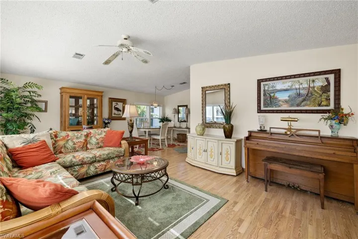 Living room with ceiling fan, light wood-type flooring, and a textured ceiling